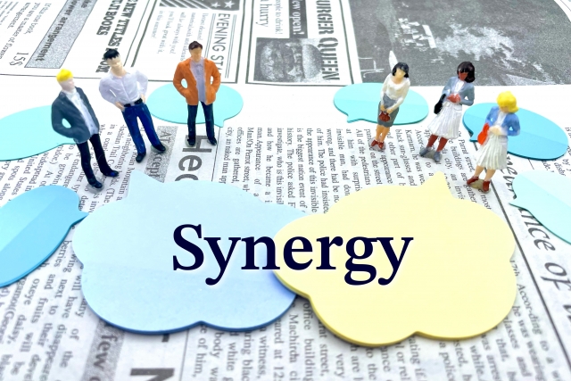 M&Aのシナジーを表すイメージ ― 雲の上に立つ人々と「Synergy」の文字