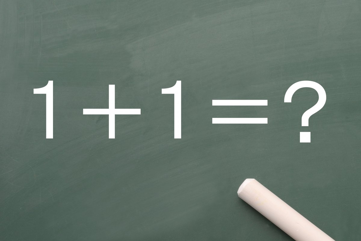黒板に書かれた「1+1=？」とチョーク ― M&Aのシナジーとは何かを問うイメージ