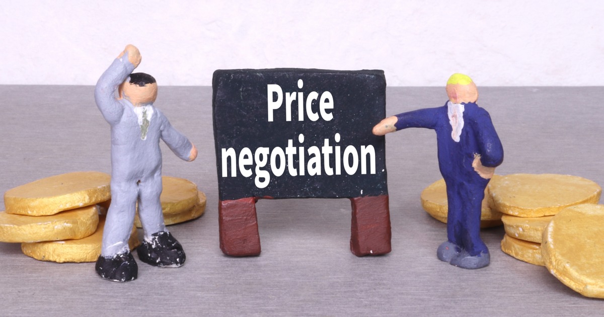 Price negotiation と書かれた黒板をはさんで向かい合う二人の人形と、両脇に積まれた金貨 ― M&Aの価格交渉を表すイメージ